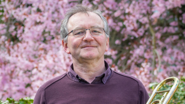 Porträt eines lächelnden Mannes mit Brille und grauem Haar in Lila Shirt vor hellem, unscharfem Hintergrund